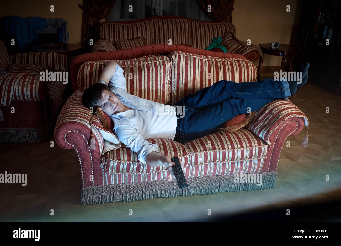 Portrait of man switching TV channels on sofa at night Stock Photo