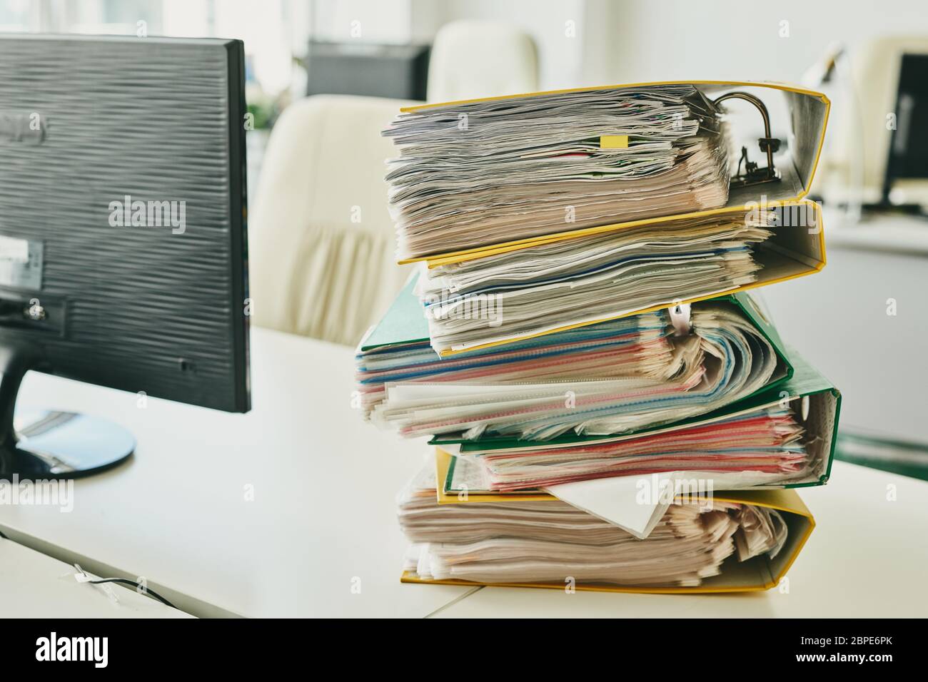 Backlog of cases after coronavirus isolation: colorful folders stacking on desk with laptop in office Stock Photo