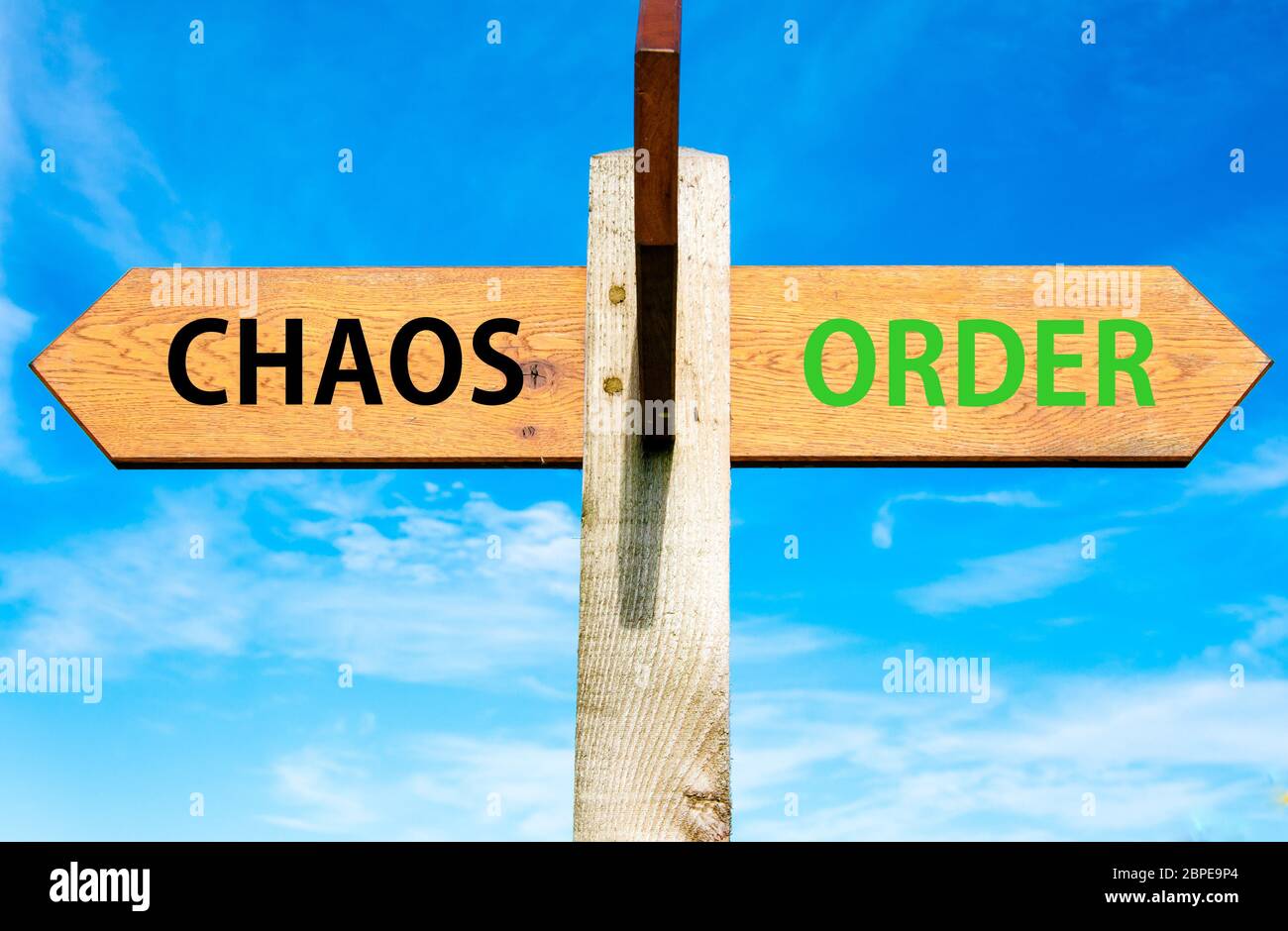 Wooden signpost with two opposite arrows over clear blue sky, Chaos versus Order messages Stock Photo