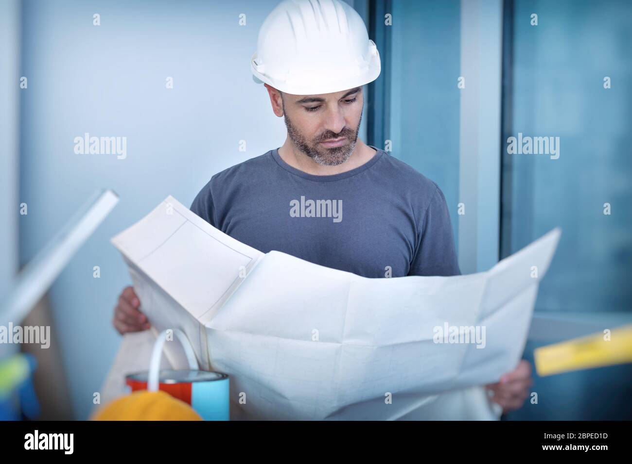 Portrait of an architect builder studying layout plan of the rooms, serious civil engineer working with documents on construction site, building and h Stock Photo