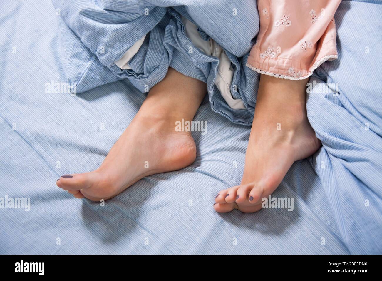Weibliche Füße mit Schlafanzug im Bett am Morgen in blauer Bettwäsche Stock Photo