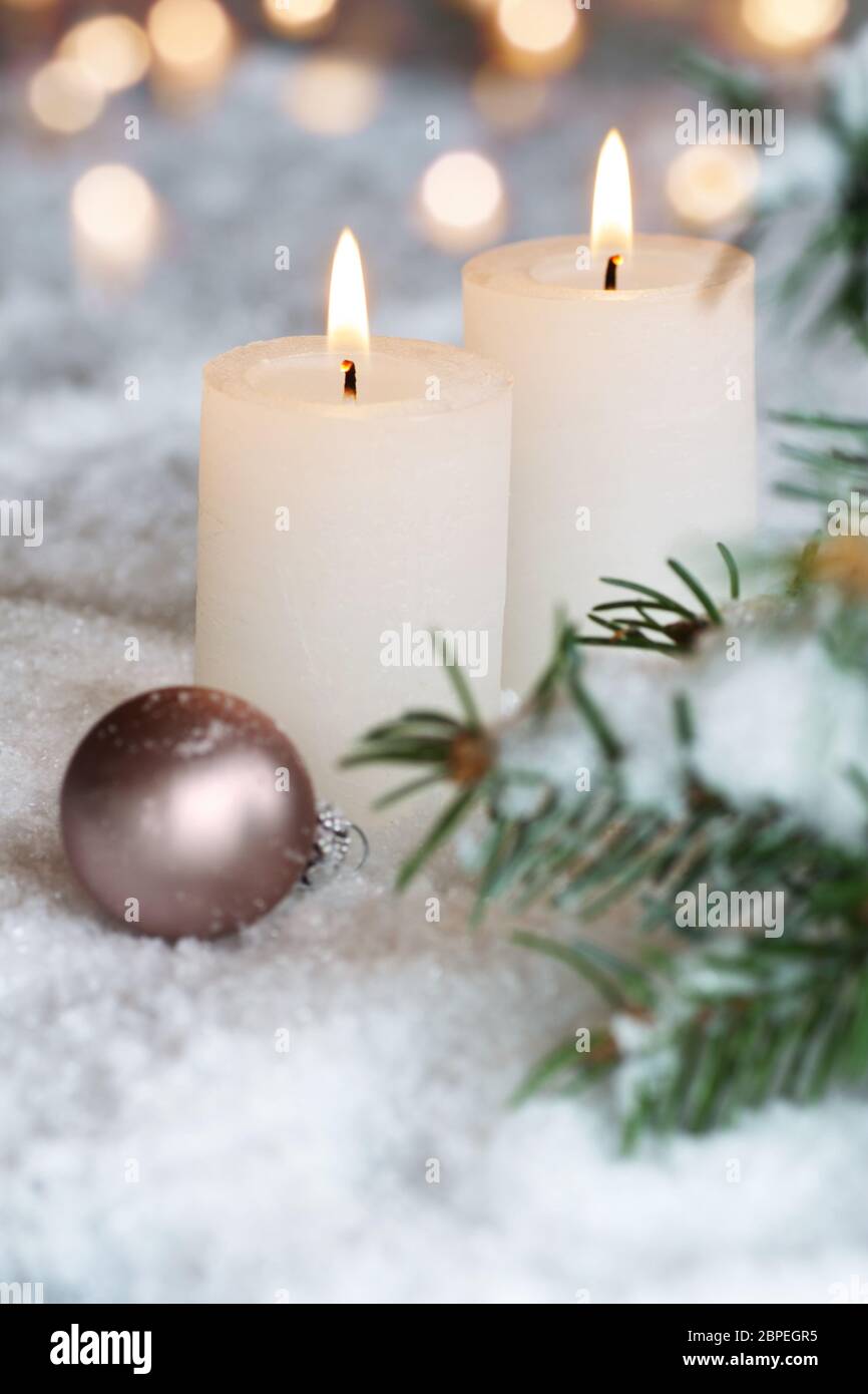 Two white Christmas candles with pine branches in the snow Stock Photo