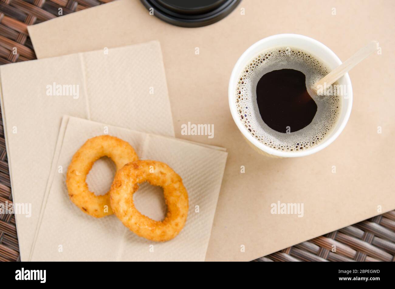 coffee in a paper cup next to onion rings on a paper napkin. Unhealthy fast food. Stock Photo