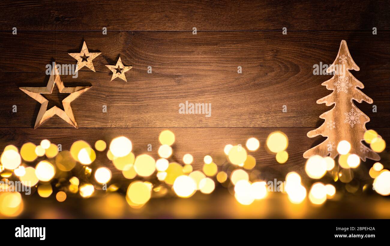Christmas background with wooden ornaments arranged on a dark wood board and bokeh lights shining in the foreground Stock Photo