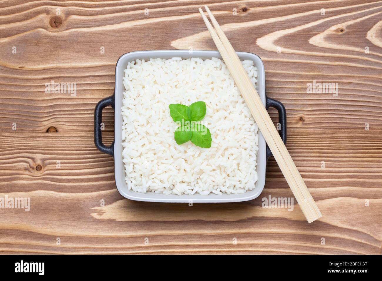 Rice with basil in ceramic bowl with chopsticks on wooden table. Top view. Stock Photo