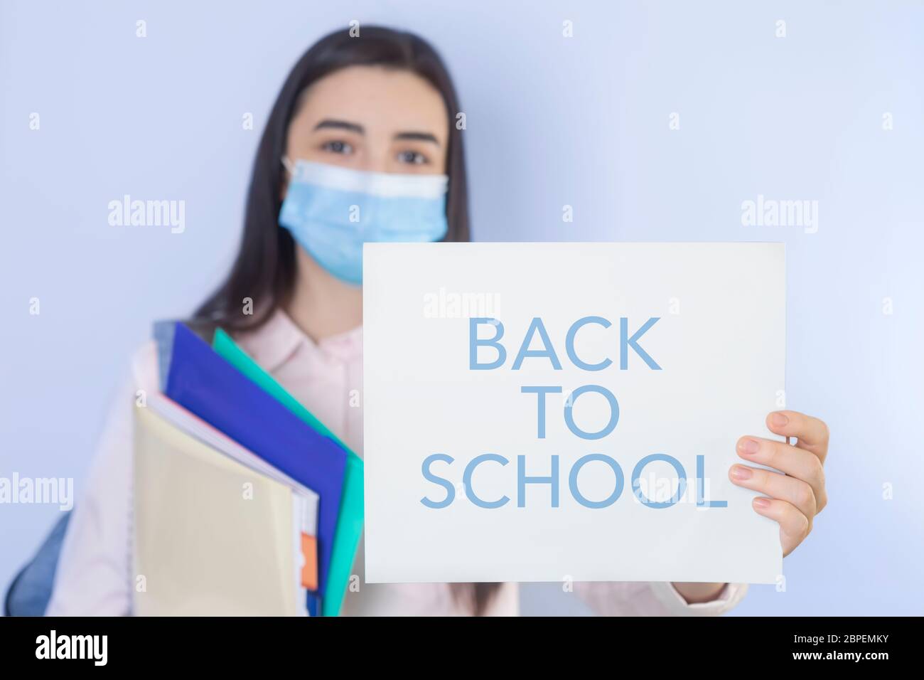 High school girl with mask on her showing back to school message. Student girl ready for school during the coronavirus pandemic. Focus on her hand wit Stock Photo