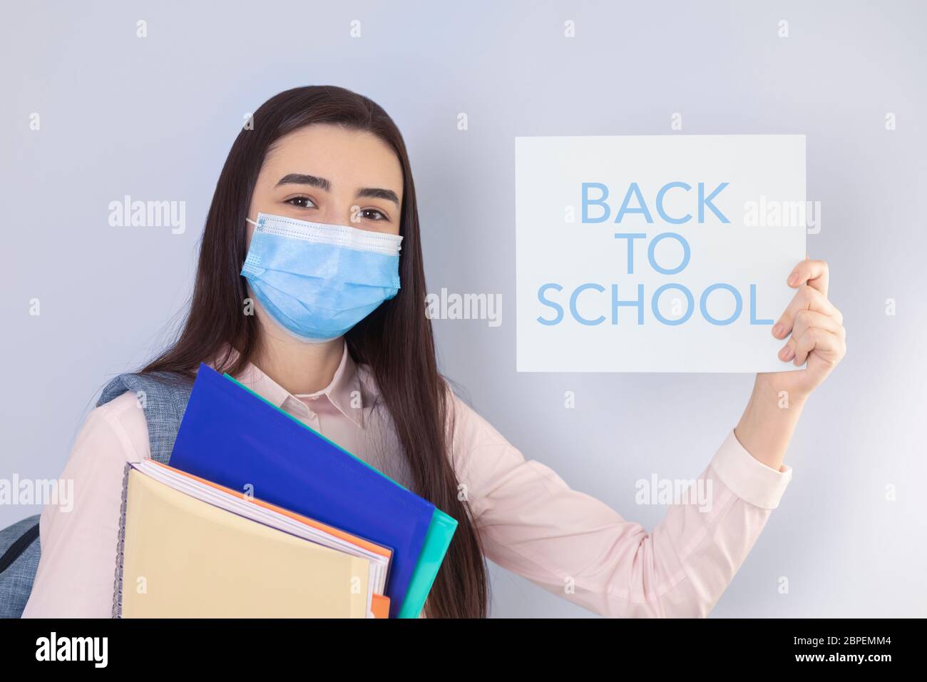 High school girl with mask on her showing back to school message. Student girl ready for school during the coronavirus pandemic. Focus on her face. Stock Photo