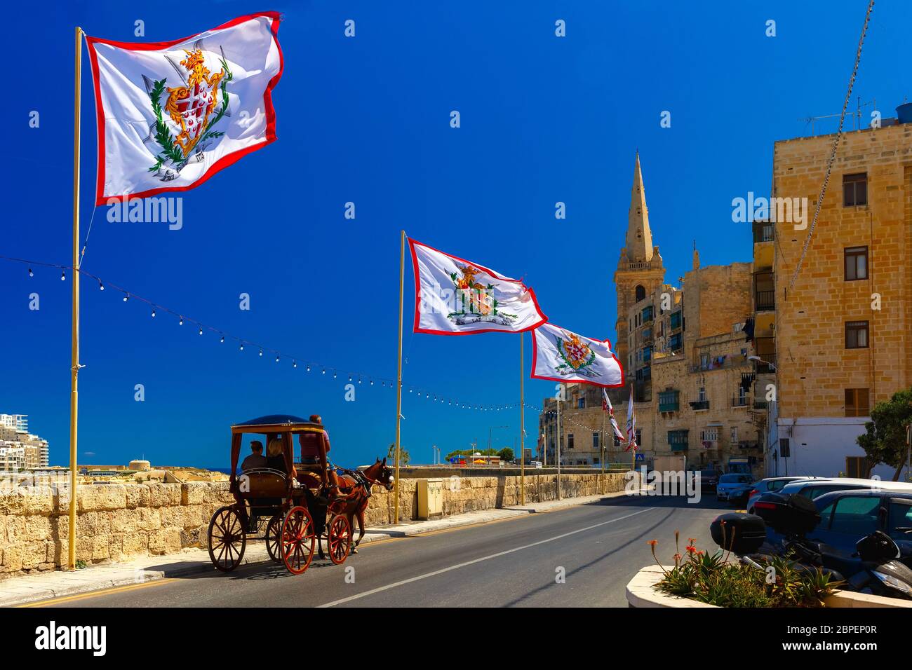 Festively decorated street with flags of all the Grand Masters of the Sovereign Military Order of Malta in the old town of Valletta, Malta Stock Photo
