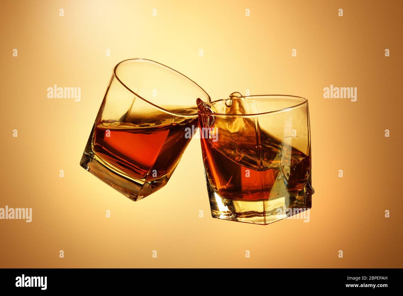 Two whiskey glasses clinking together on brown studio background Stock Photo