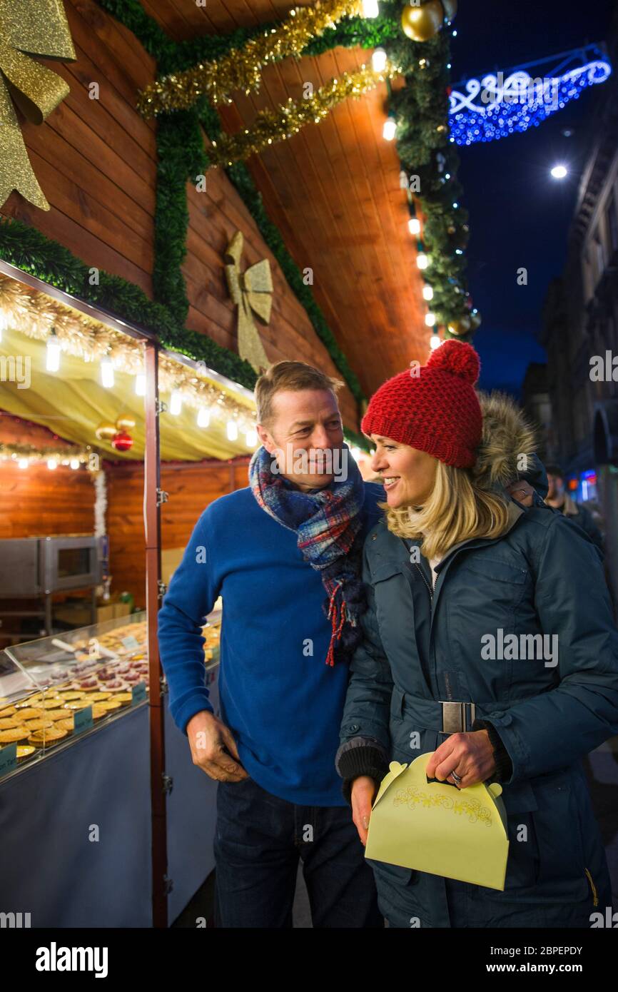 Mature couple are looking at a french pattisserie stall together in the city christmas market. Stock Photo