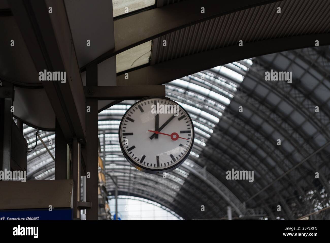 Eine Bahnhofsuhr mit der Deckenstrukur eines Bahnhofs im Hintergrund Stock Photo