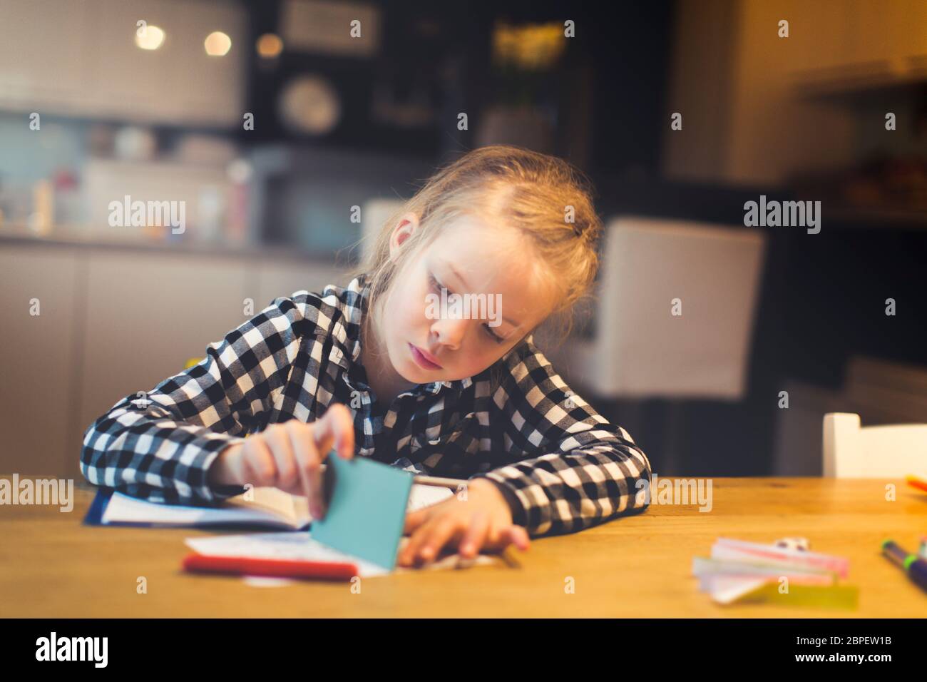 beautiful, blond girl is sitting at the table and is doing schoolwork at home Stock Photo