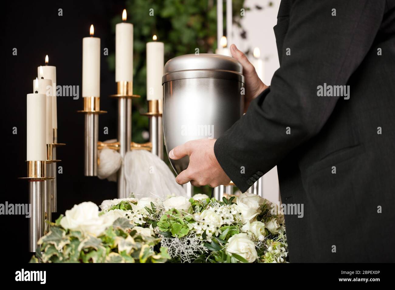 death and dolor  - funeral and cemetery, mortician carrying the urn to a bed of white roses Stock Photo