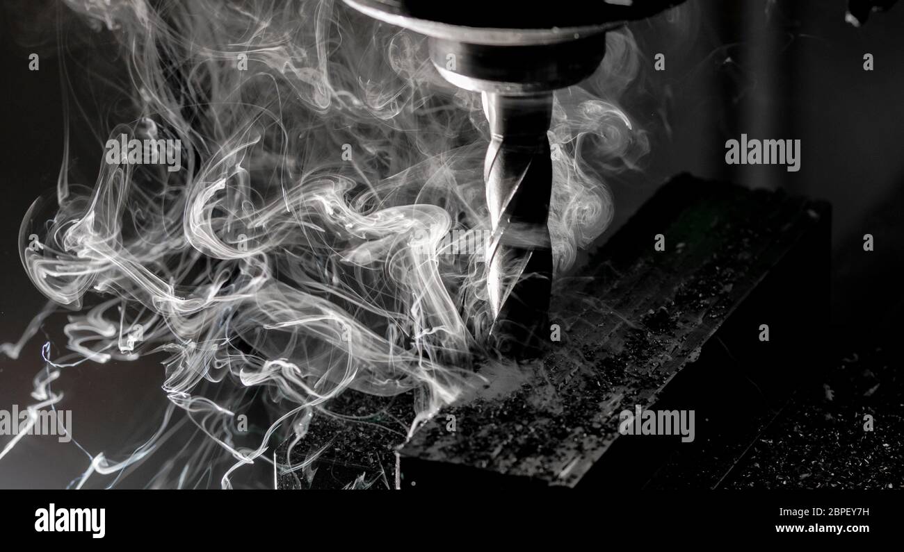 Bridgeport CNC end mill finishing a stack of steel plate with metal filings chips and heavy smoke trailing Stock Photo