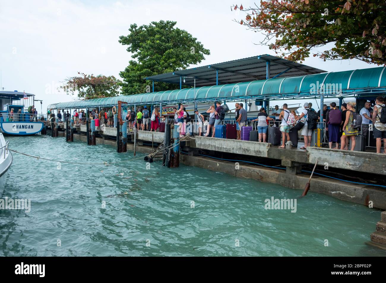 Ko Pha-ngan / Thailand - February 2020: Tropical island pier with tourists and boat. tourists waiting to board the Haad Rin Queen ferry at Haad Rin Stock Photo