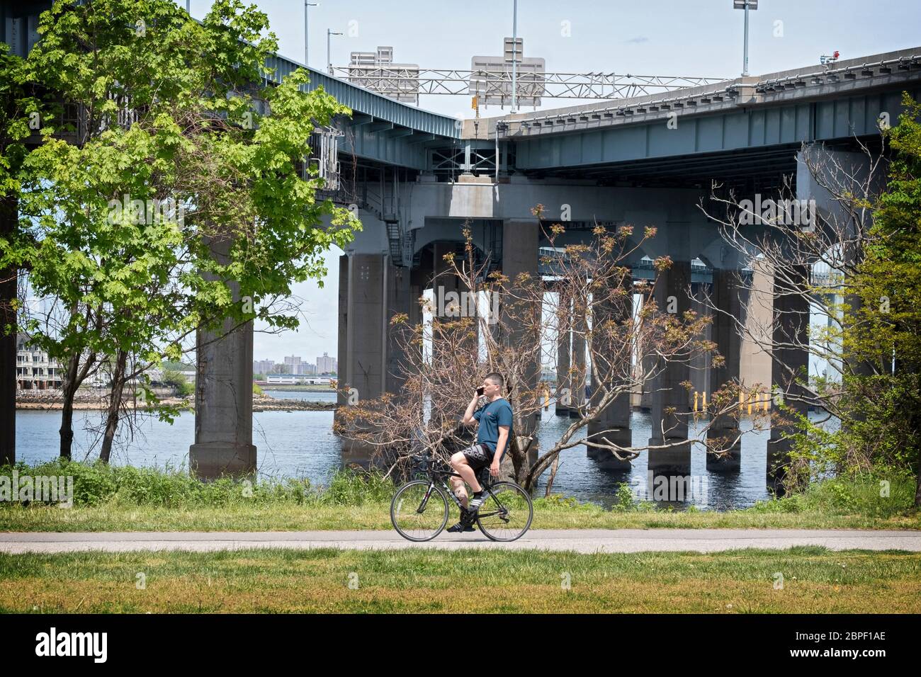 A biker rides while talking on the phone in Little Bay Park in front of the entrances to the Throgs Neck Bride. in Whitestone, Queens, New York. Stock Photo
