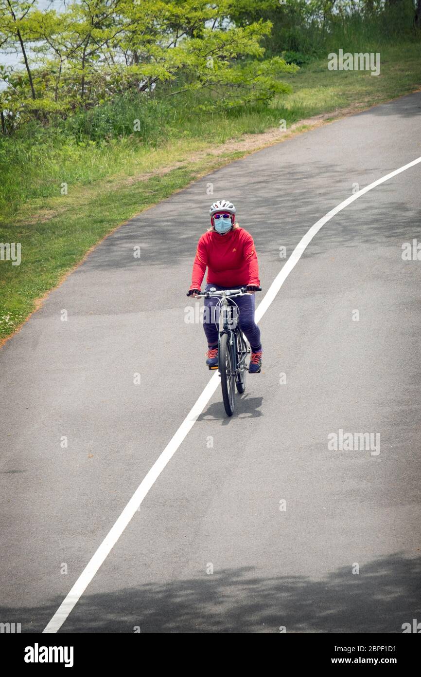 A woman cyclist wearing a surgical mask during the coronavirus plague. On the path near the Bayside Marina in Bayside, Queens, New York City Stock Photo
