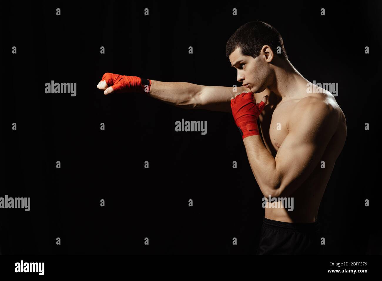 Sportsman boxer practicing side kick. Red bandages on the hands