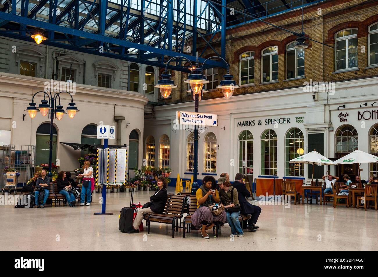 Passengers waiting in Brighton Railway Station in front of shops Stock