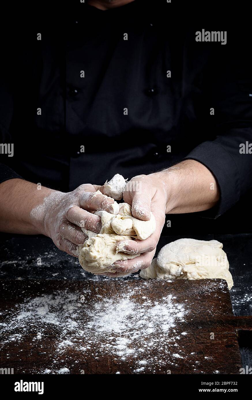 baker kneads white wheat flour dough on a brown  wooden table Stock Photo
