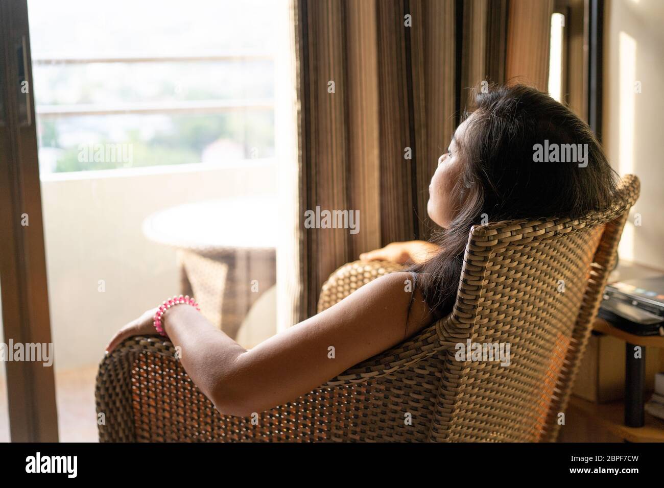 Concept image of the issues surrounding mental health.A woman sitting in a chair stares out of an open window during a quarantine period in the COVID-19 Pandemic 2020 Stock Photo