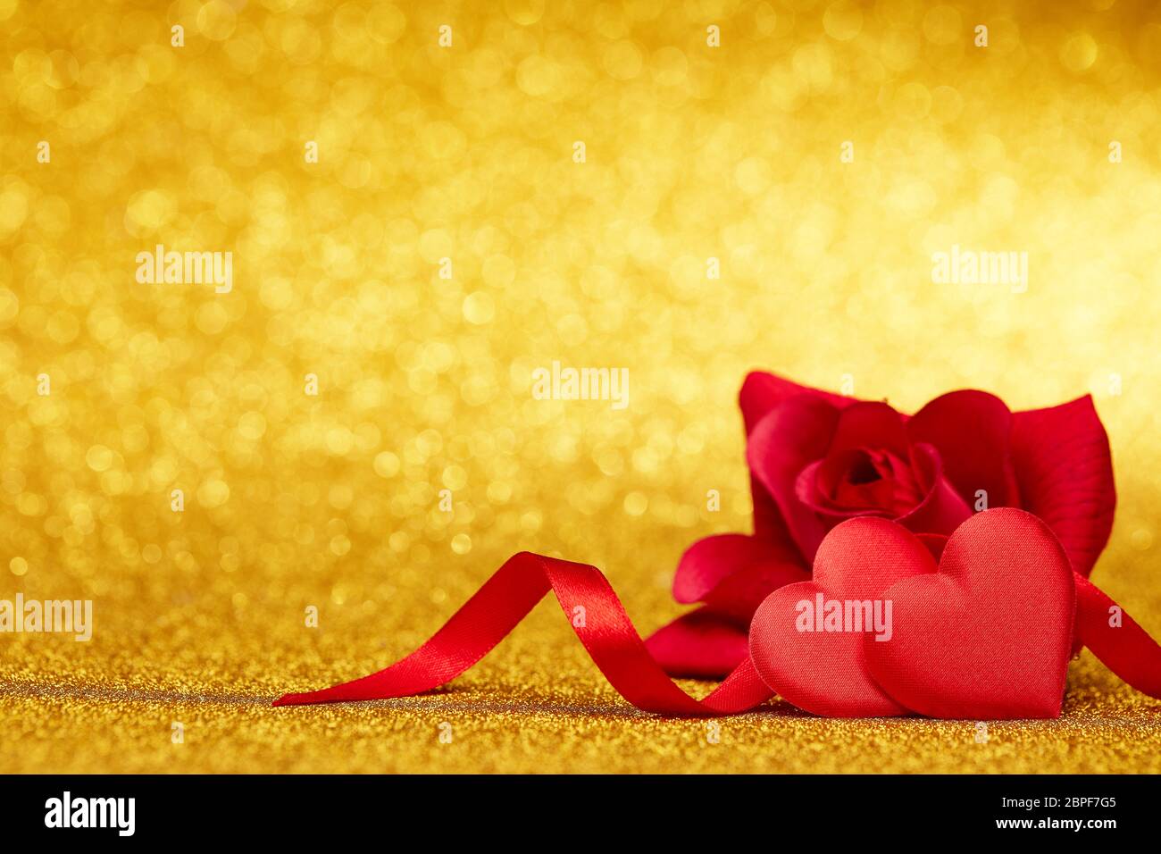 Two decorative hearts and red rose on a glittering gold background with ...