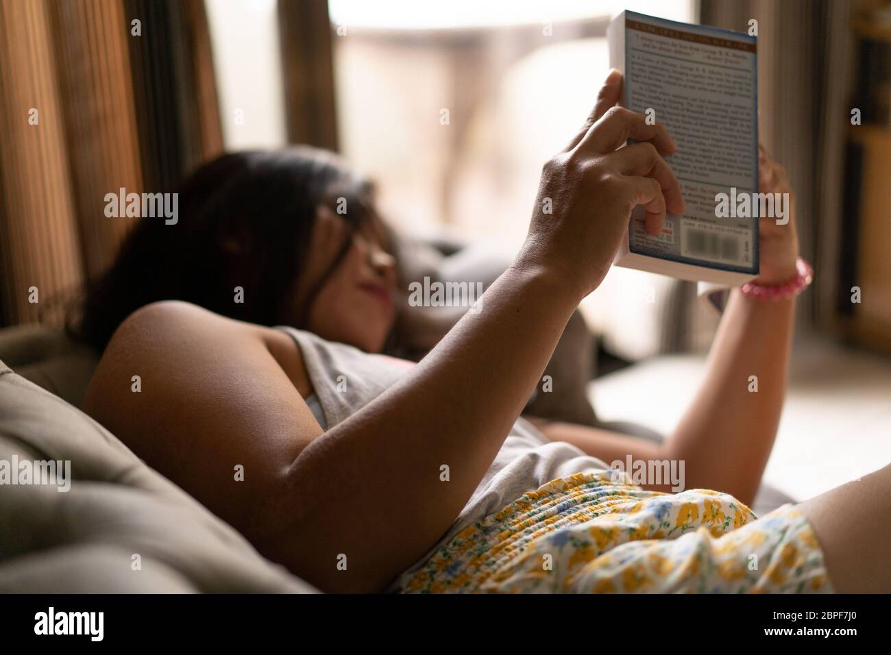 a woman  lying on a settee reading a book during a quarantine period in the COVID-19 Pandemic 2020 Stock Photo