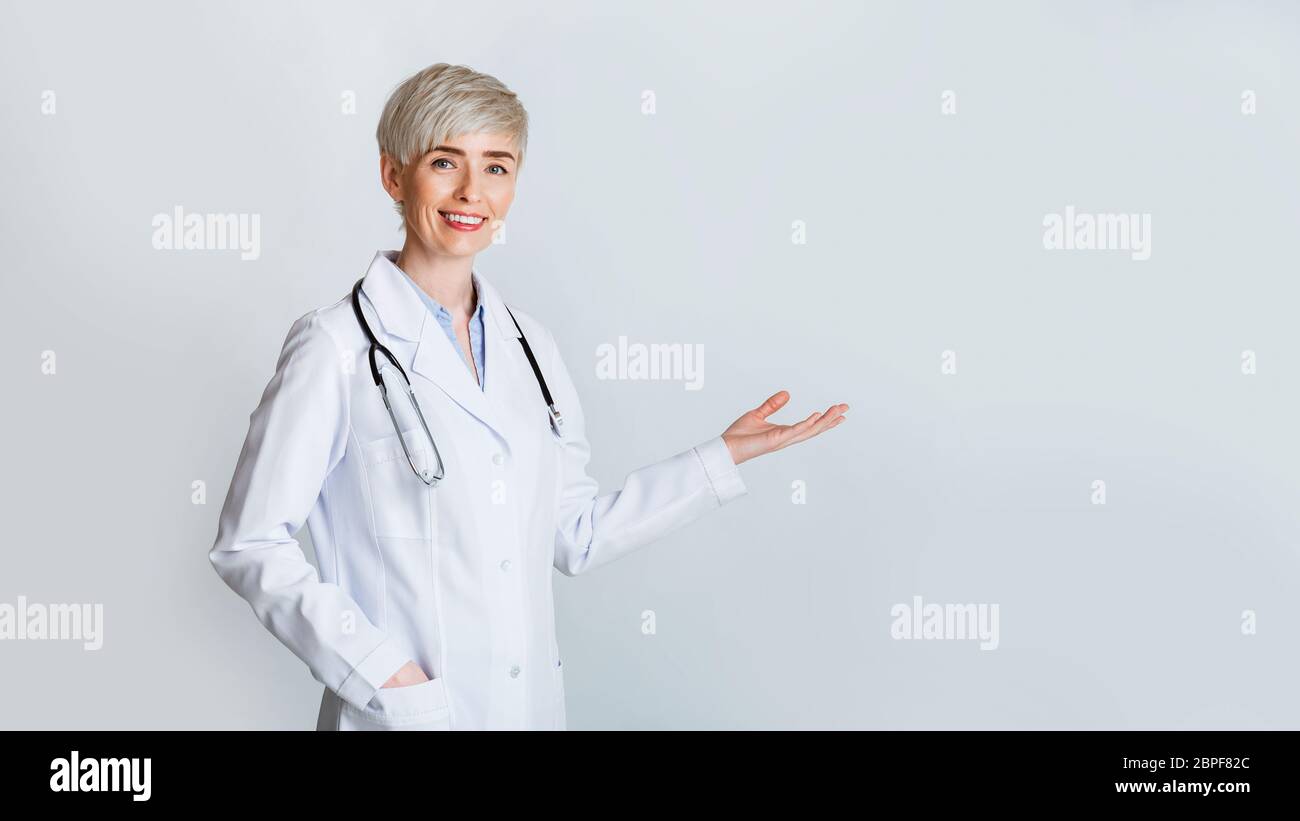 Woman invites to meet. Smiling doctor in white coat shows gesture welcome Stock Photo
