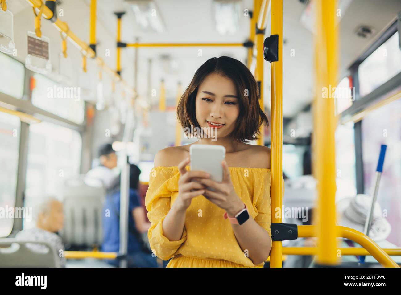 Young attractive woman using mobile while standing on the bus/ public transportation. Stock Photo