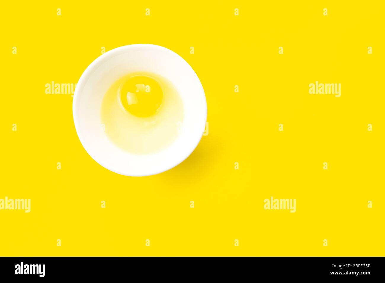 Raw egg in bowl on yellow background. Healthy food and cooking at home concept. Stock Photo