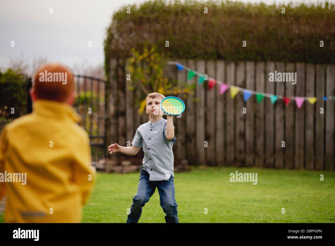 Two young boys playing outside in a back garden. They are throwing a