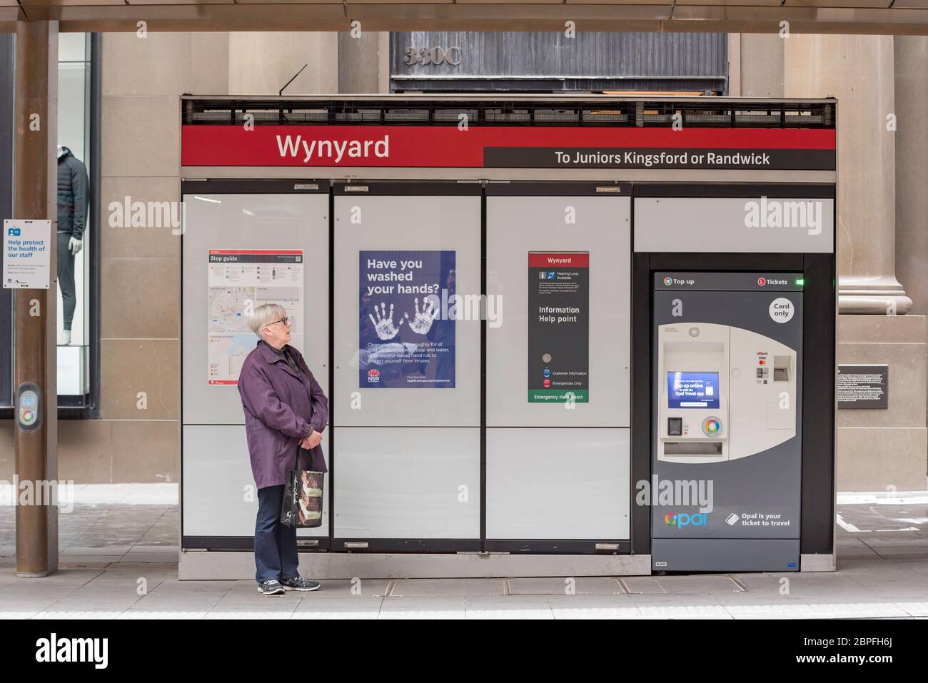 A lone woman passenger waits beside a government issued 'Have you washed your hands?' sign at a light rail stand in George Street, Sydney, Australia Stock Photo