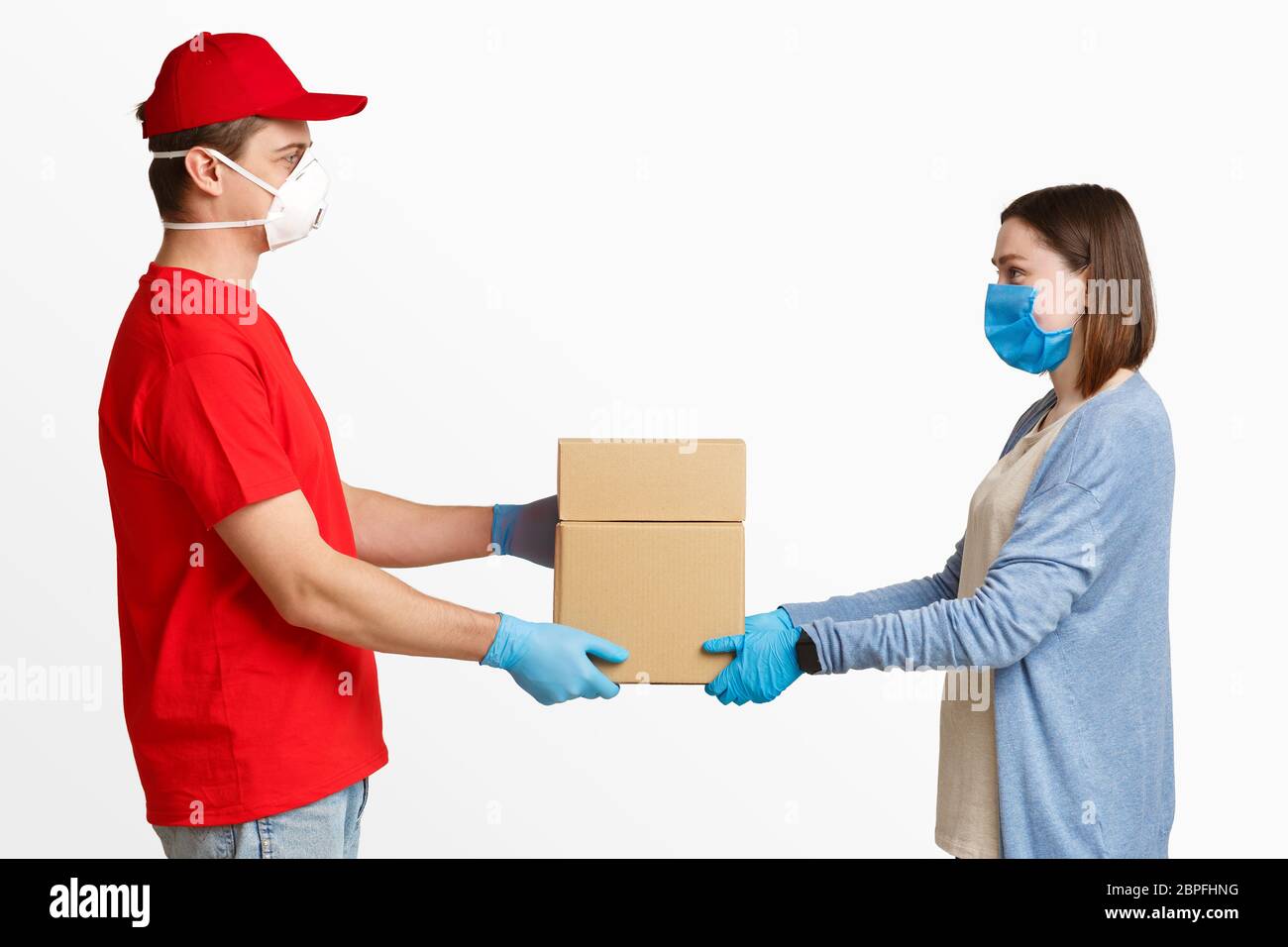Delivery to door during quarantine. Courier gives parcel to girl in mask Stock Photo