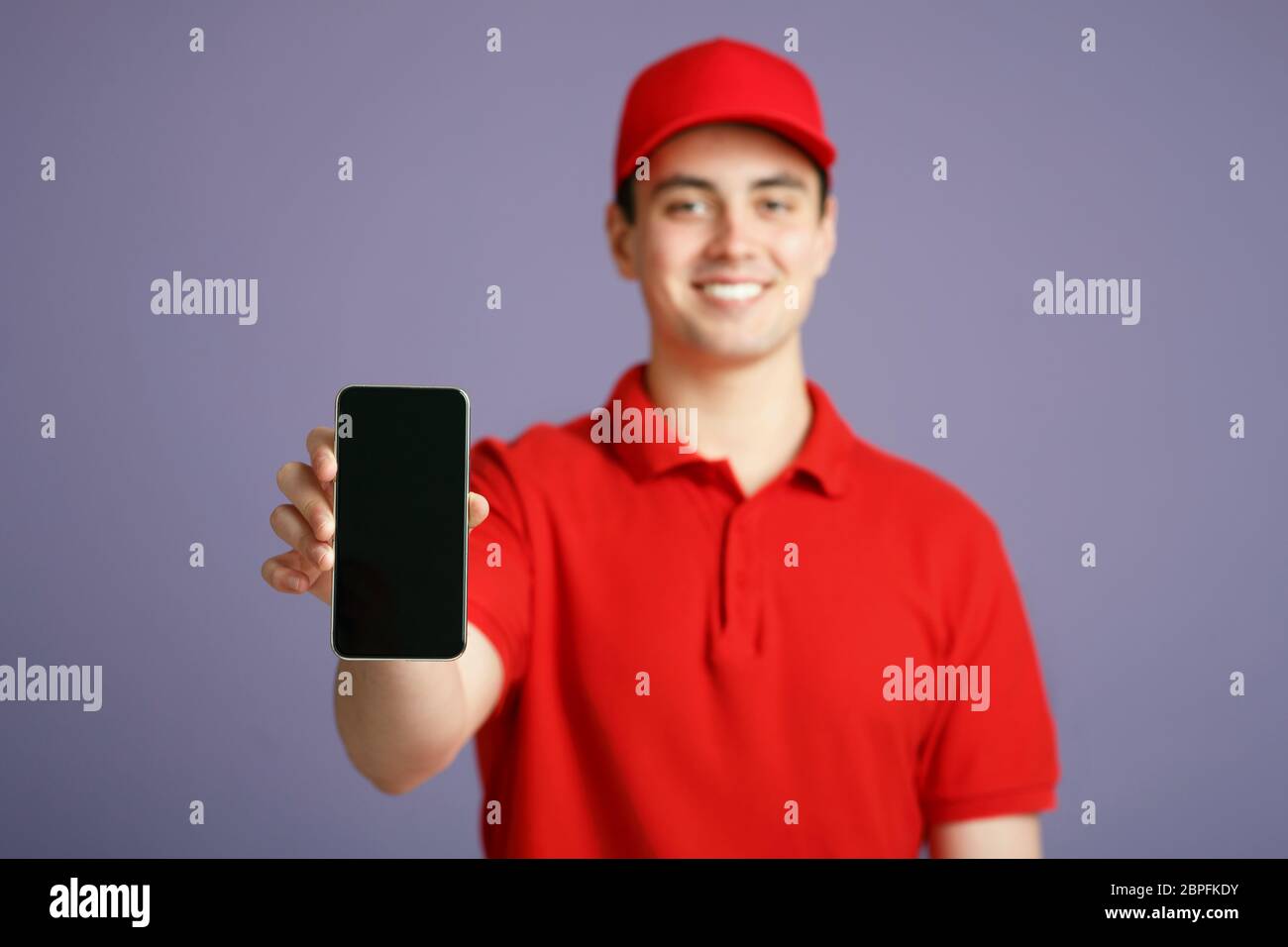 Courier in red uniform shows on camera smartphone with blank screen Stock Photo
