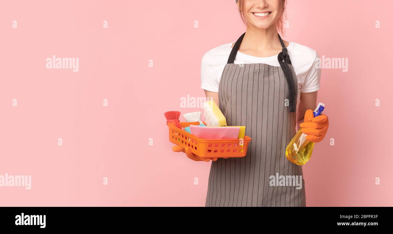 Domestic cleaning services. Smiling housemaid in apron with household supplies in hands Stock Photo