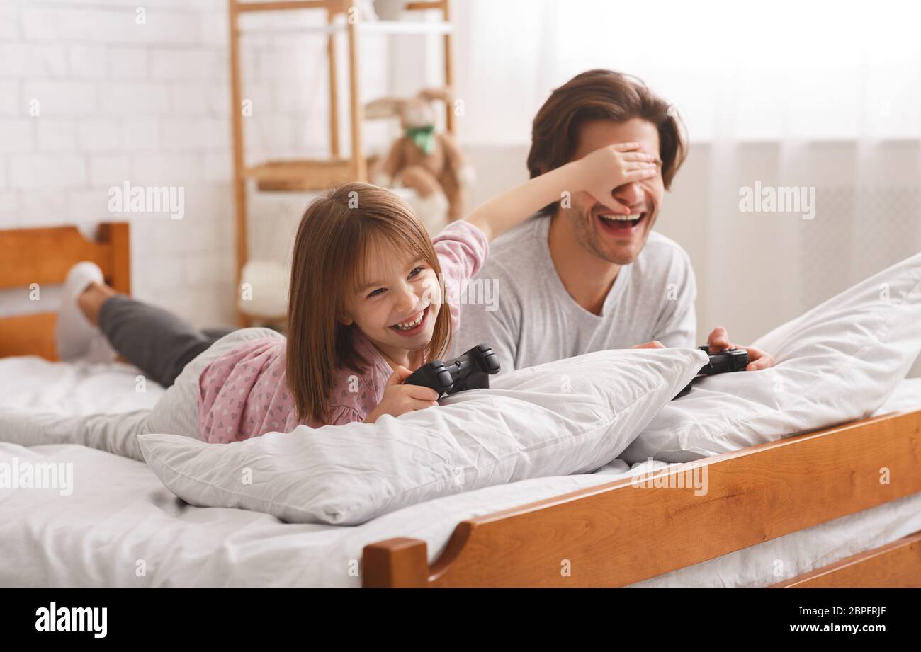 Playful girl covering her dad eyes while playing videogame Stock Photo