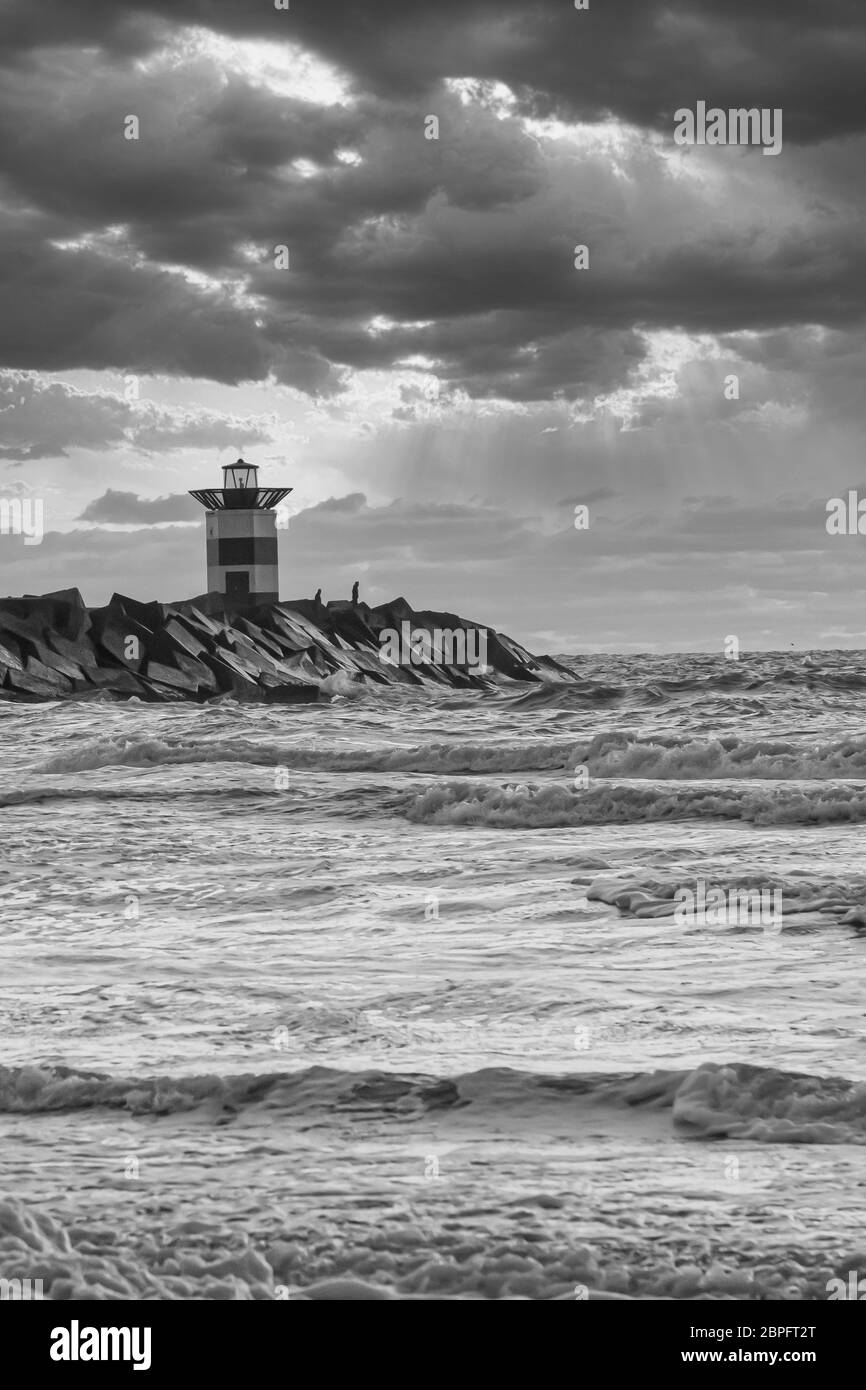 Striped Lighthouse During A Vibrant Sunset Water Hits The Black Boulders In Waves Black And White Dramatic Sky Scheveningen The Netherlands Stock Photo Alamy