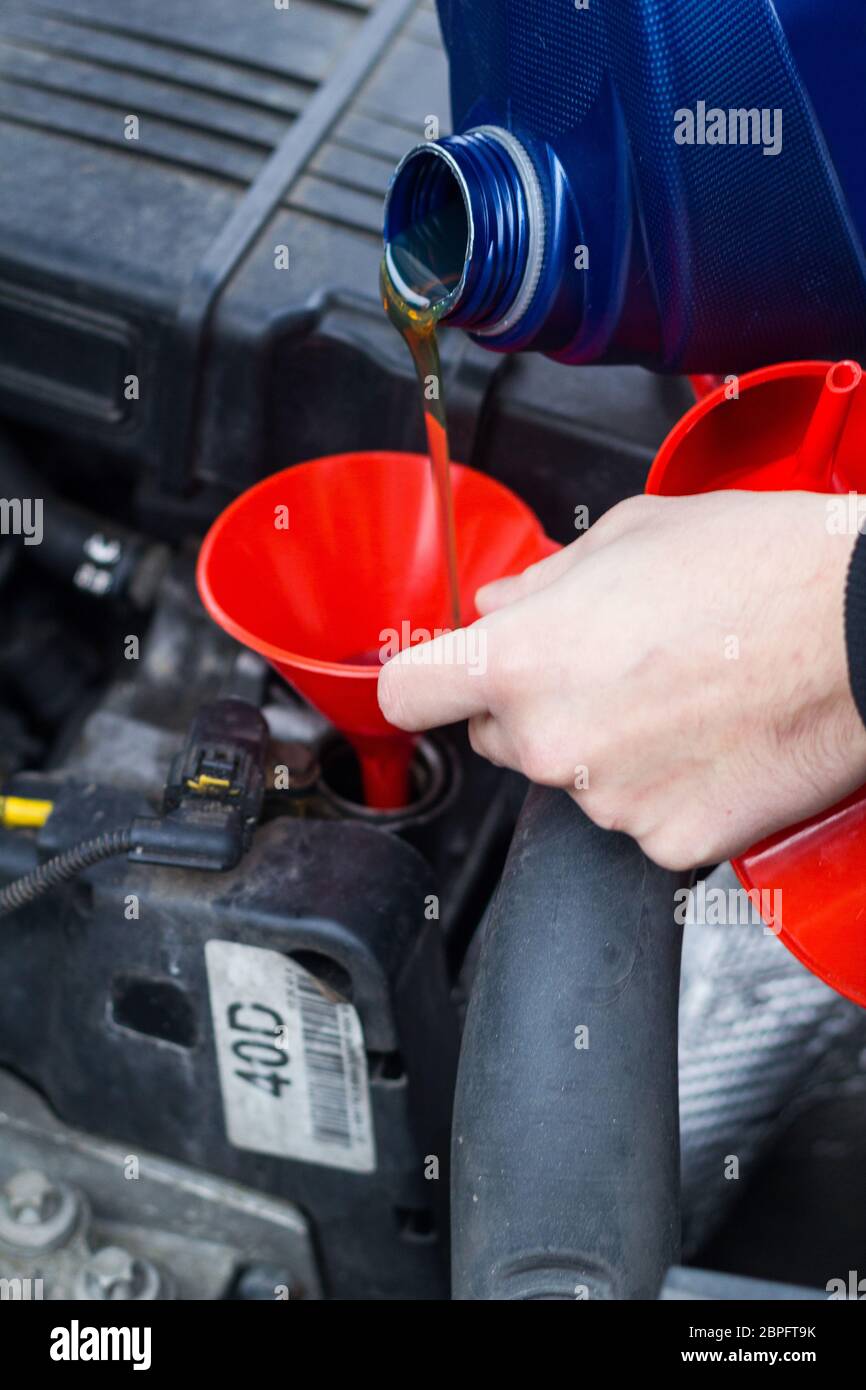 Man uses a red funnel to fill the engine oil in a car with a blue