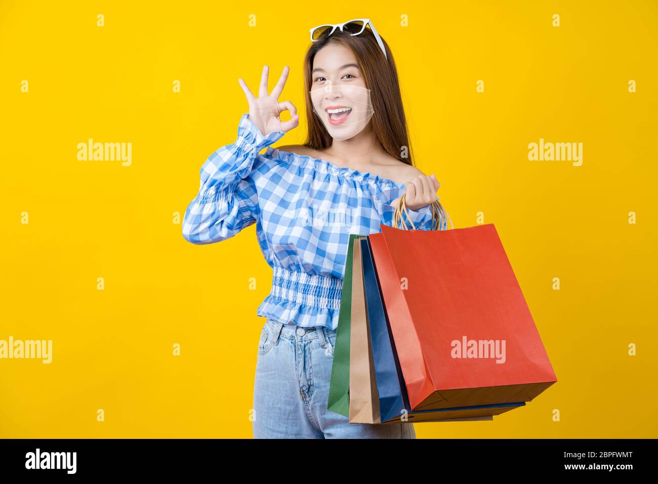 Attractive Asian smiling young woman  wearing technology augmented reality surgical mask in covid19 outbreak and Carrying a shopping coloful bag and g Stock Photo