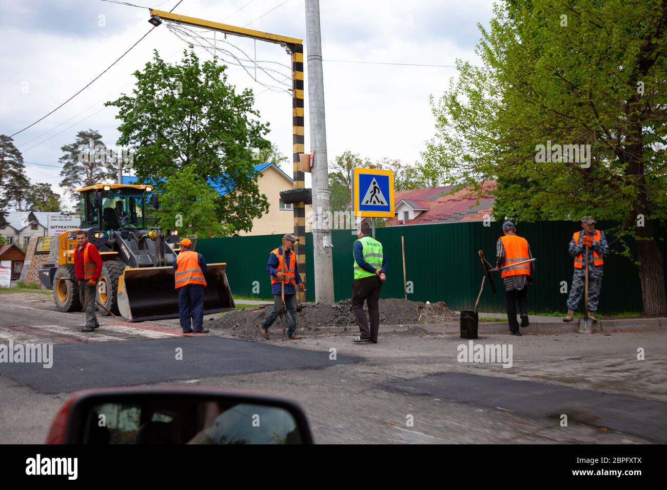 Bucha, Ukraine - May 18, 2020: Road workers. Road repair on the street. Paving asphalt and patching pits on the roads. Men in bright vests work on the Stock Photo