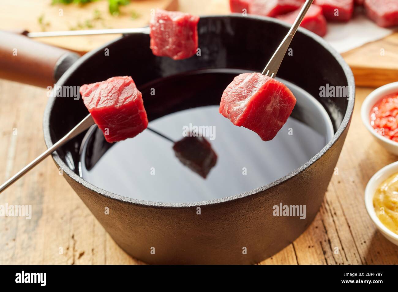 Traditional meat fondue with diced raw beef held ready on forks over