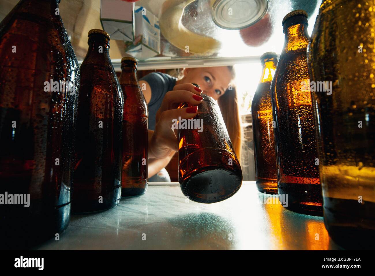 Caucasian woman takes cold refreshing beer from out the fridge, inside