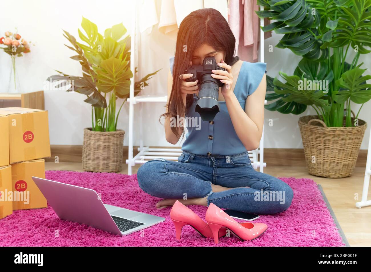 Asian woman take photo of shoe, fashion accessories for upload and selling online on website with many parcel box for shipping delivery. Stock Photo
