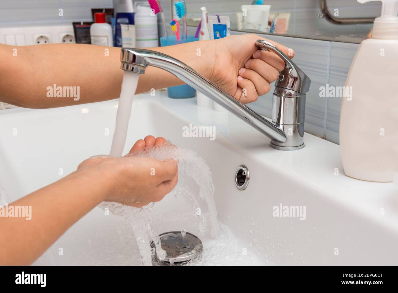 The child opens the faucet in the bathroom, and adjusts the warmth of the water Stock Photo