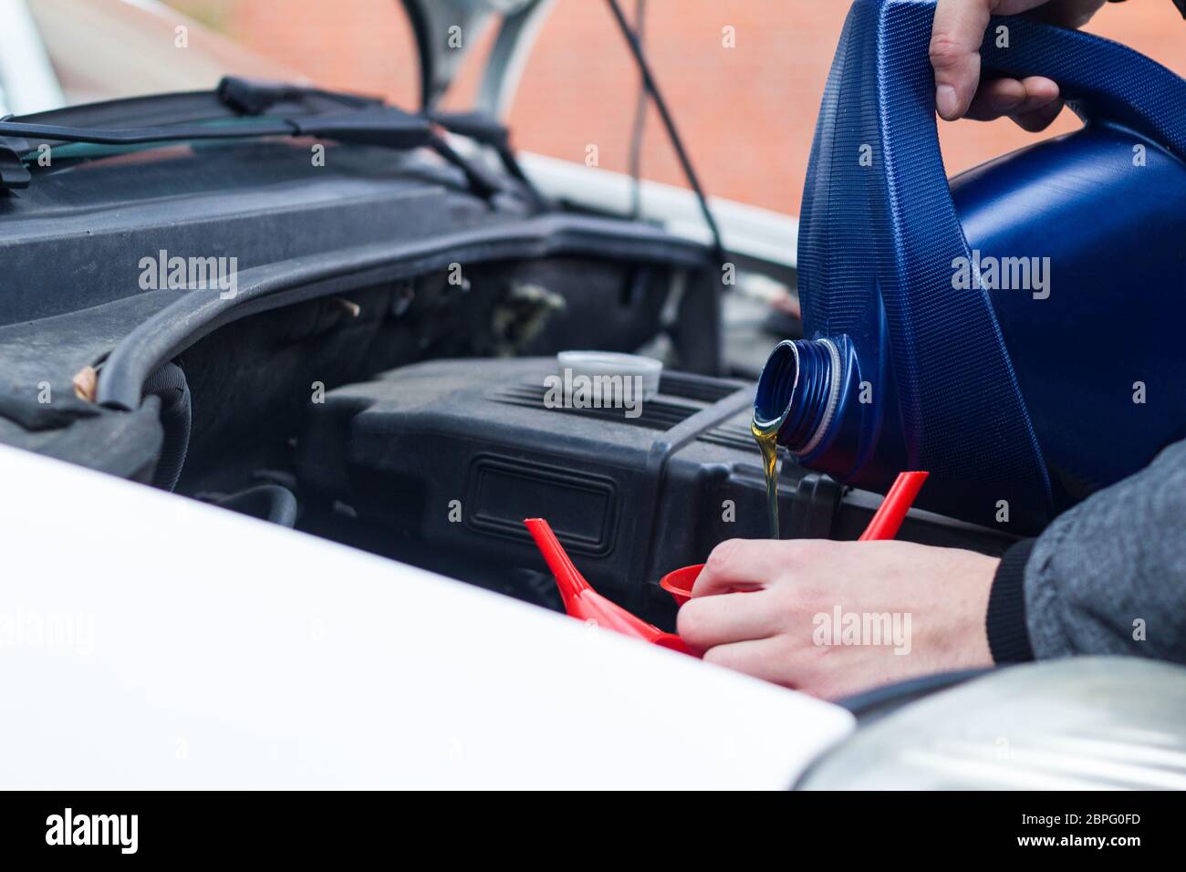 Man uses a red funnel to fill the engine oil in a car with a blue canister. Mechatronic oil level expert e-mobility Stock Photo