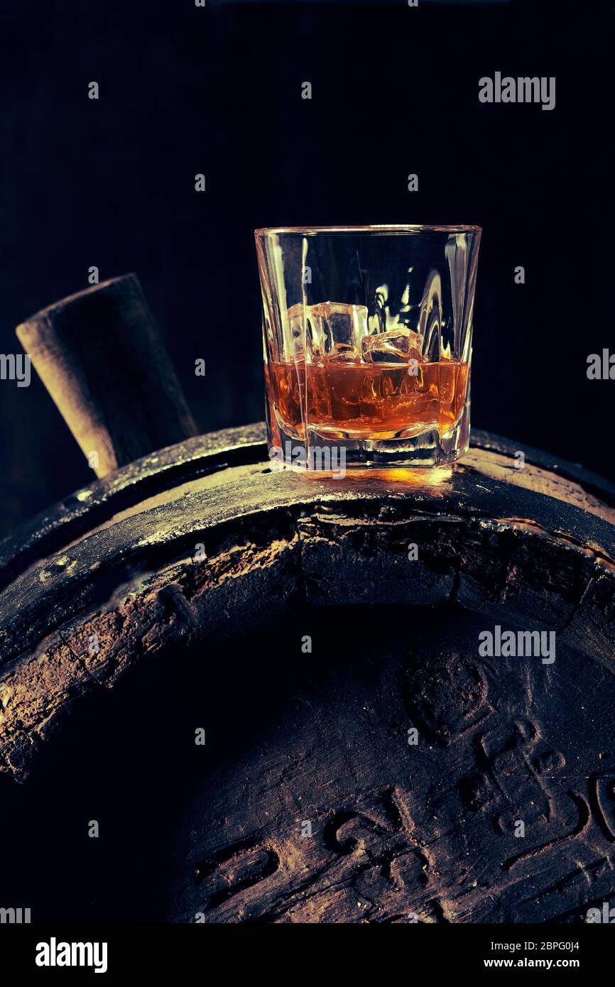 Glass of scotch whiskey with ice on dark old barrel with markings