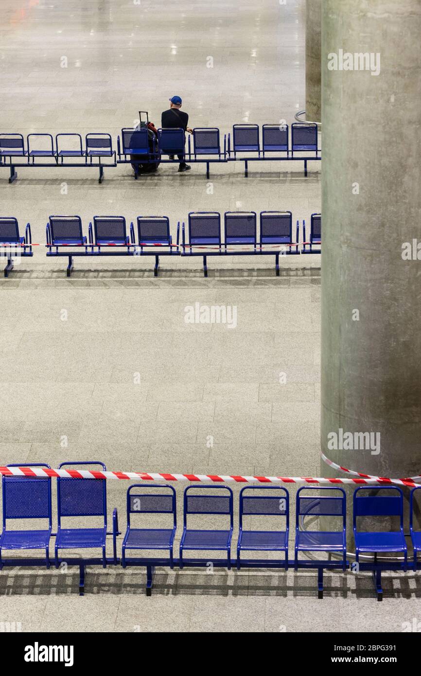Lonely passenger in empty airport terminal during a coronavirus pandemic. Stretched protective red tape on the chairs. Strong decline in passenger tra Stock Photo