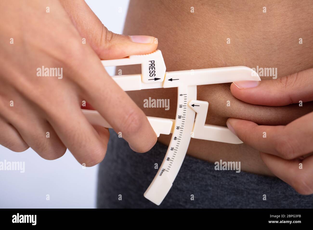 Closeup Of A Slim Woman Using Fat Caliper To Measure Body Fat On Waist