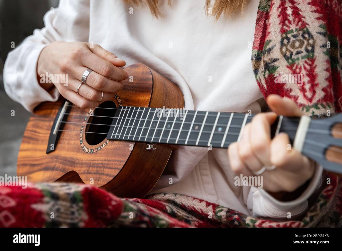 Woman playing Hawaiian guitar, sings a song on vintage ukulele at home. Selective focus. Close up. Stock Photo
