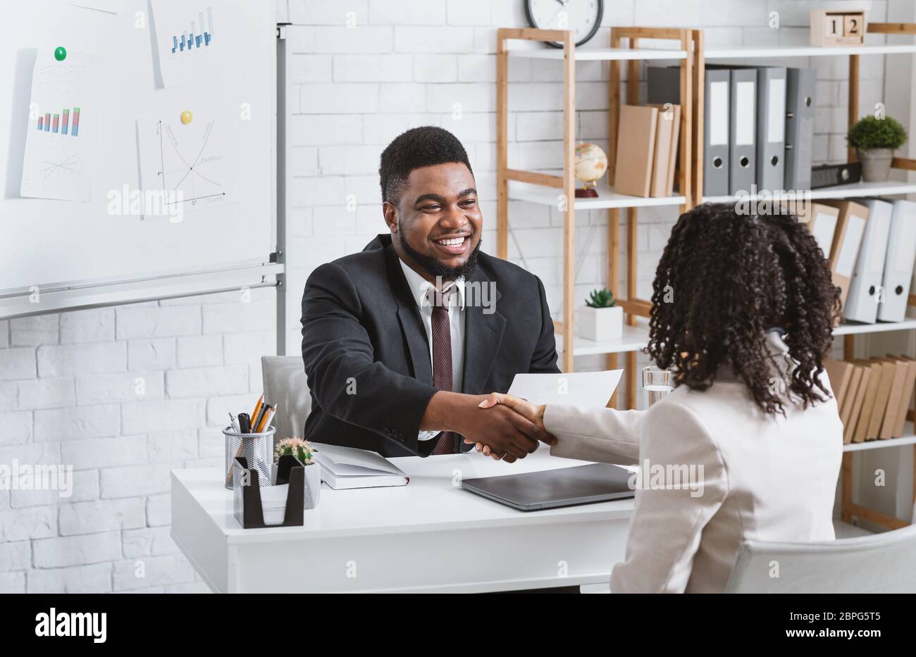 Personnel manager and young job applicant shaking hands at modern company office Stock Photo